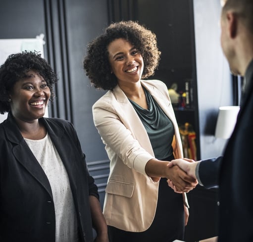 woman shaking a man's hand with another woman standing next to her