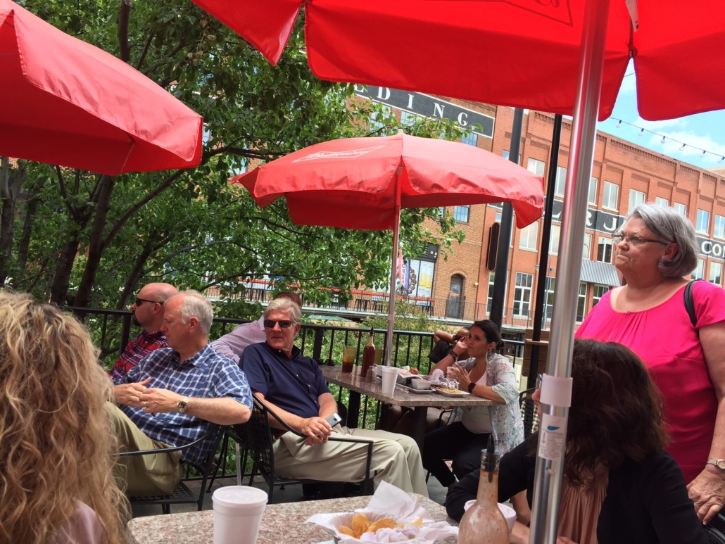 members sitting at tables under red umbrellas