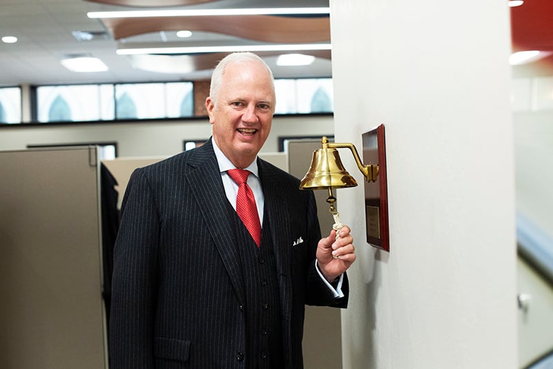 tony caldwell standing in a hallway ringing a gold bell