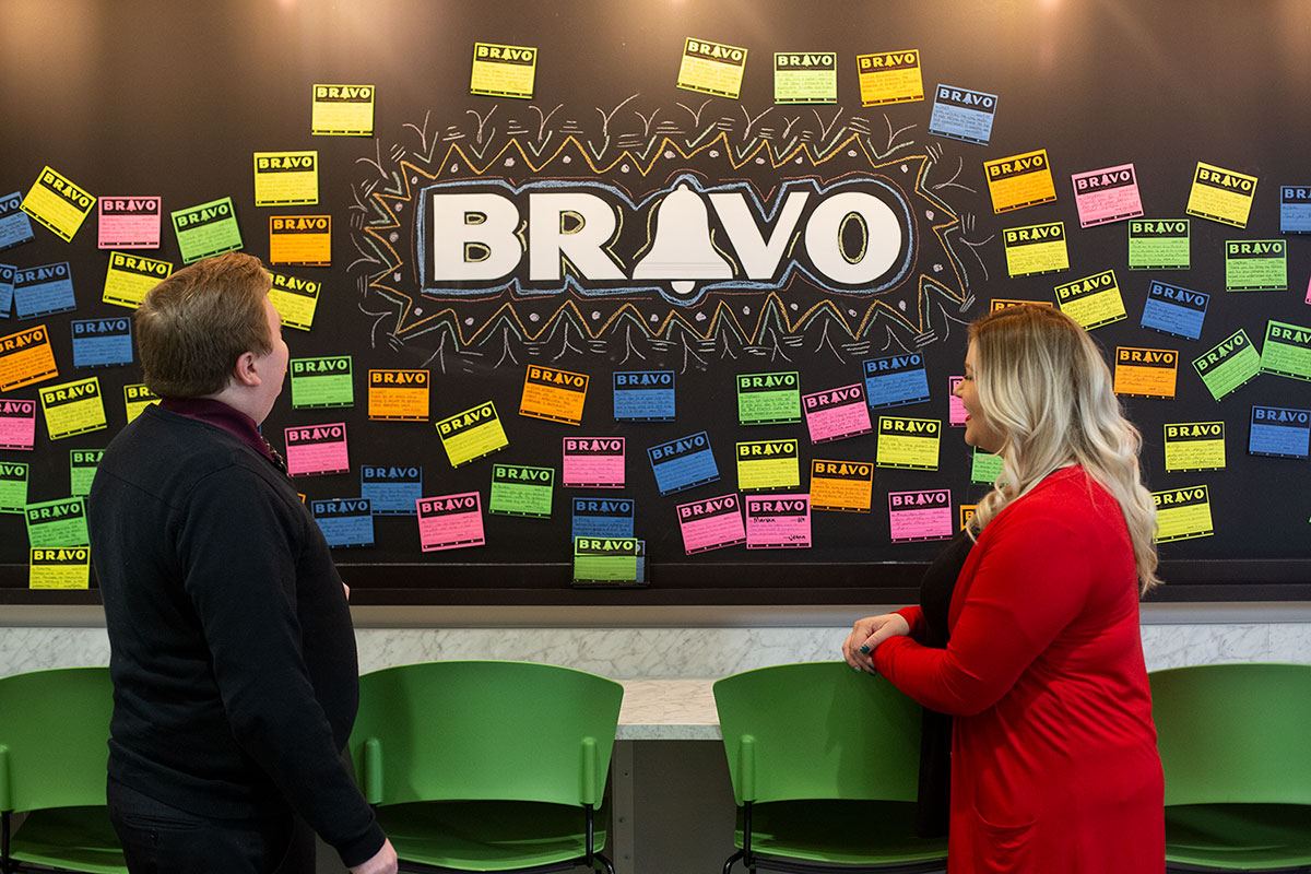 Two OAA staff members reading notes on the Bravo recognition board in the office
